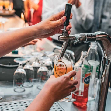 Hand zapft ein Glas Bier an einem Zapfhahn.