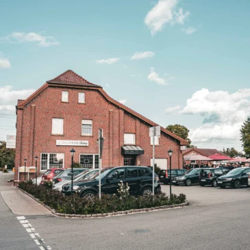 Außenbereich mit Parkplatz, Sonnenschirmen und Gästeeingang.