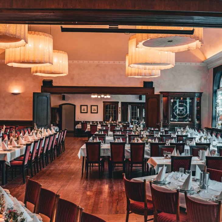 Großer Festsaal mit langen Tafeln, weißen Tischdecken und Lampen.