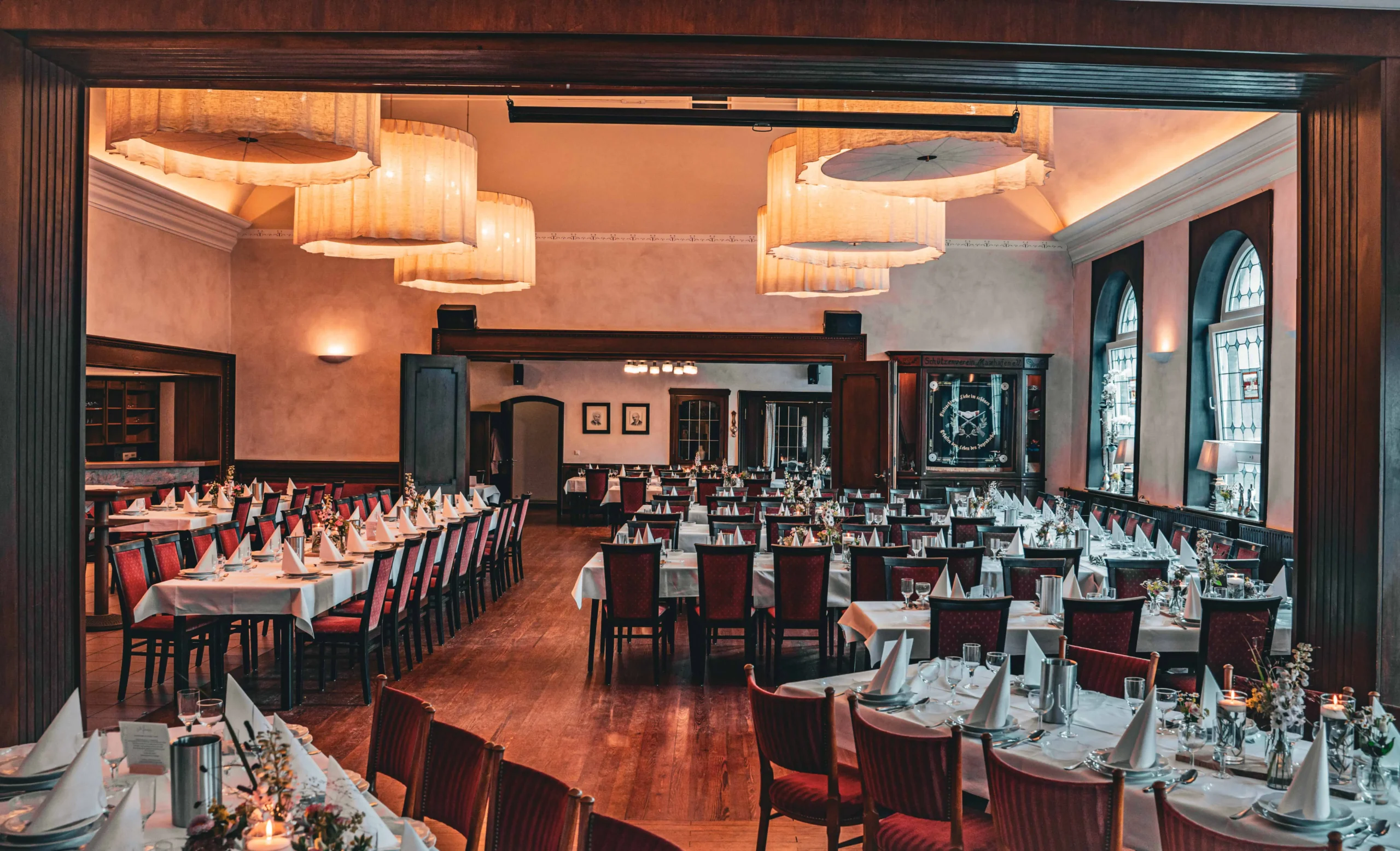 Großer Festsaal mit langen Tafeln, weißen Tischdecken und Lampen.