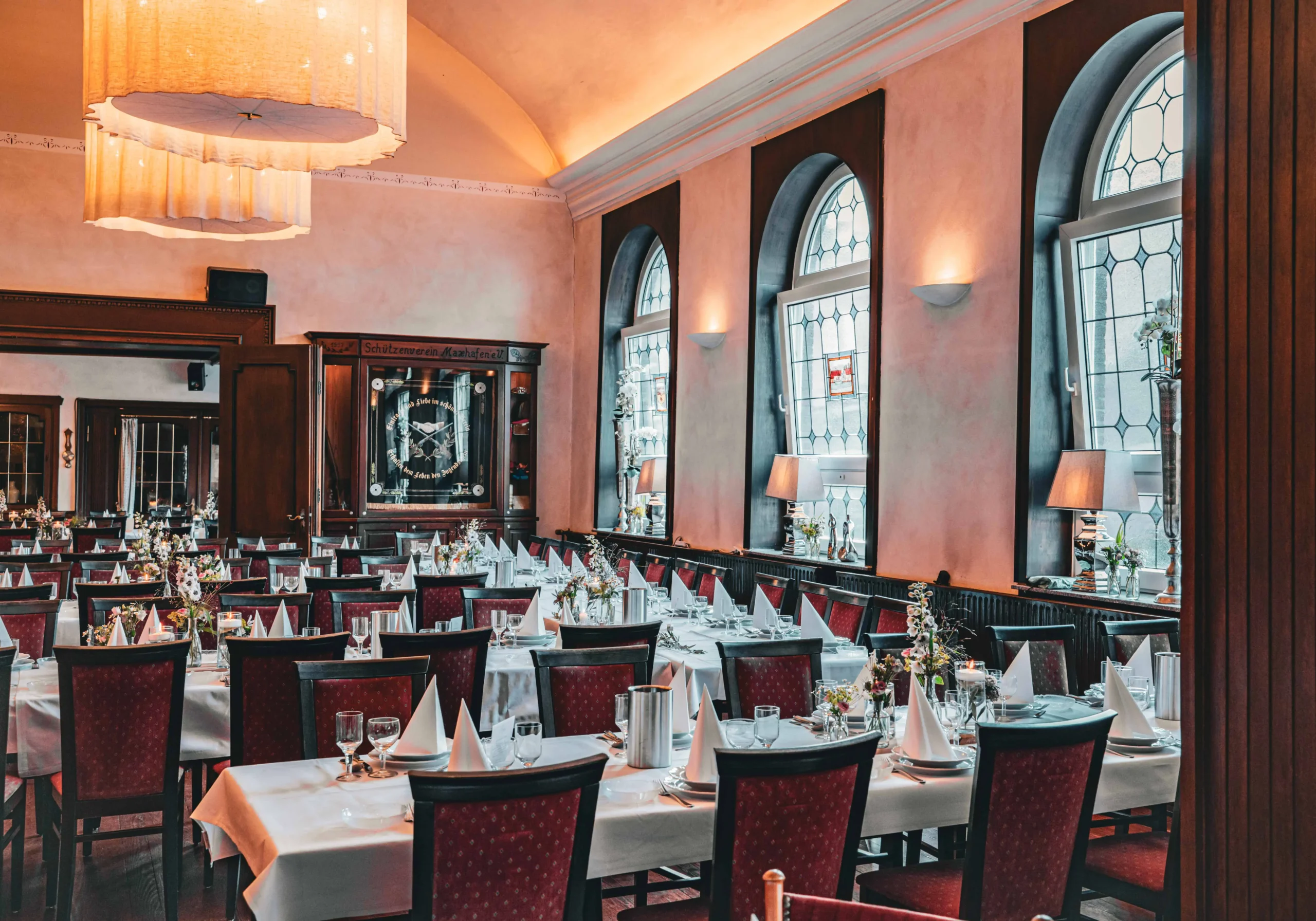 Gedeckte Tische vor großen Fenstern in einem großen Saal.